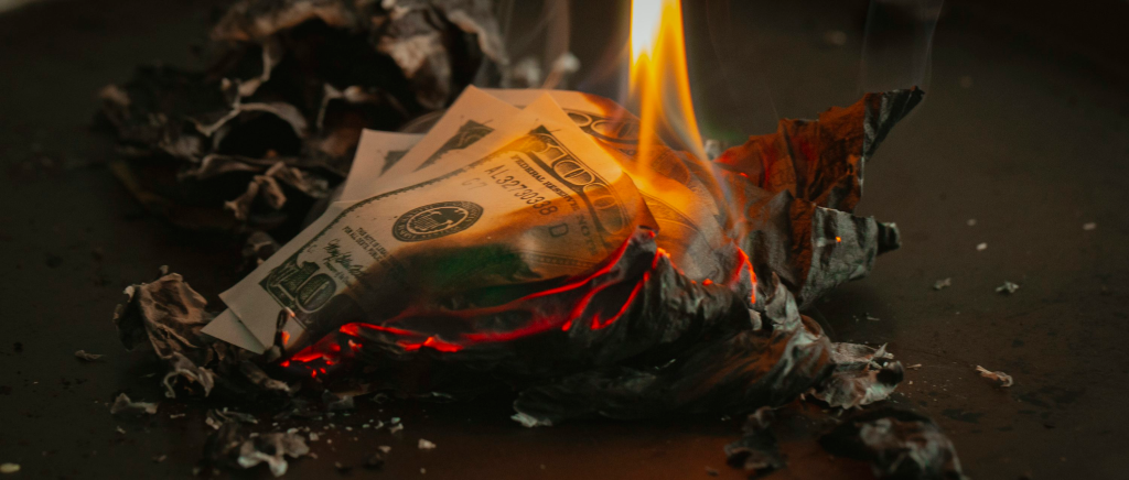 Nota de cem dólares queimando, ilustrando a mecânica de Investimento e Queima de recursos em Centavos Macabros.